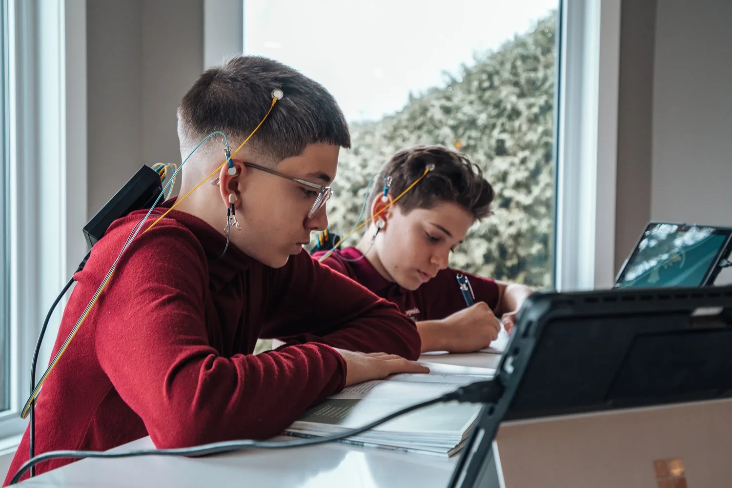 Two young boys doing neurofeedback sessions at home while they study at a desk near a window.